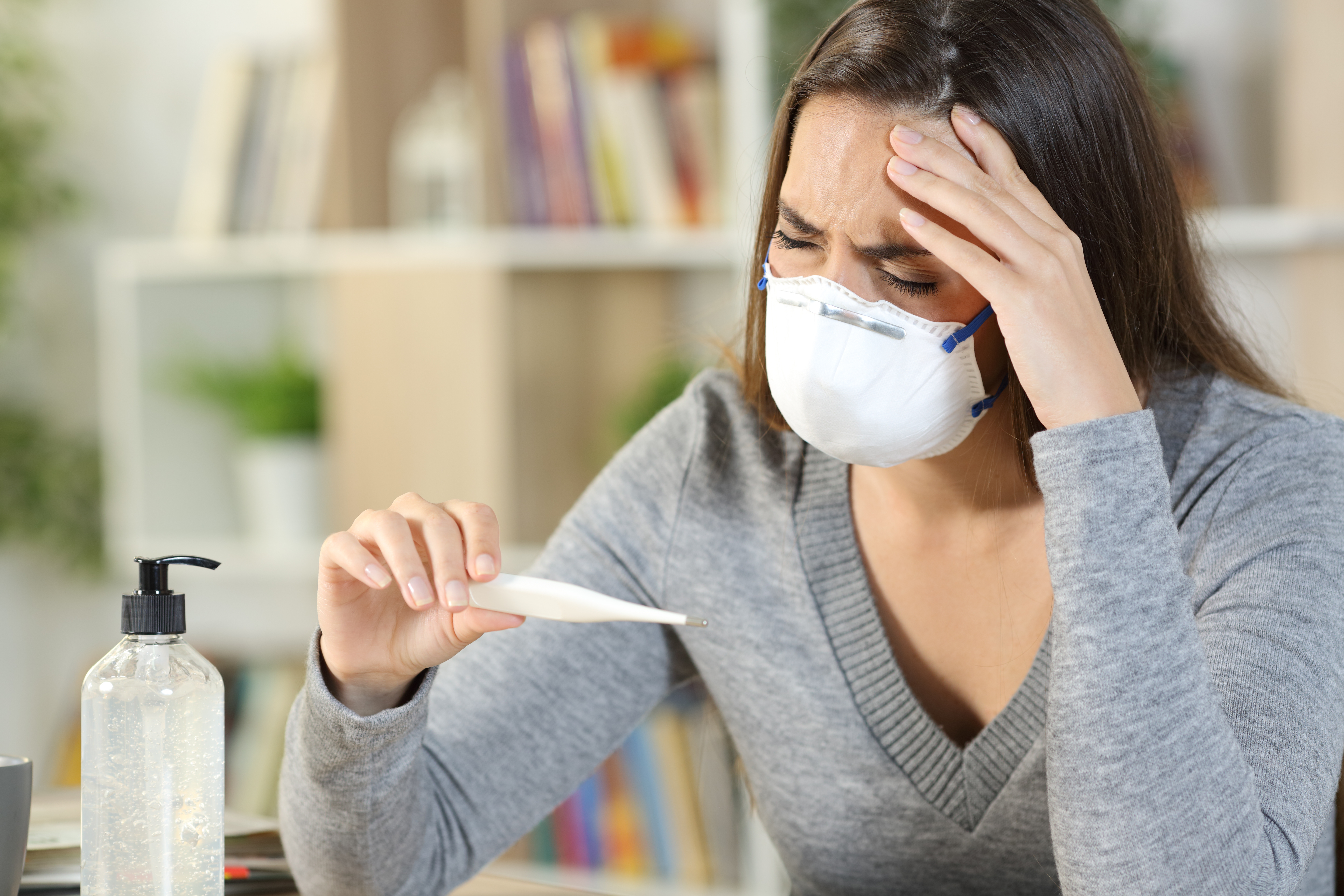 Sick woman with covid-19 symptoms holding thermometer at home