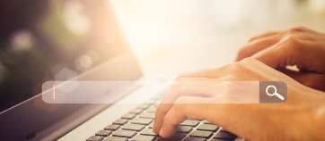 A person types on a laptop keyboard. A search bar appears in the foreground. 