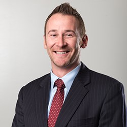 Jason Chaplin from mid-chest up in a black business suit and red tie