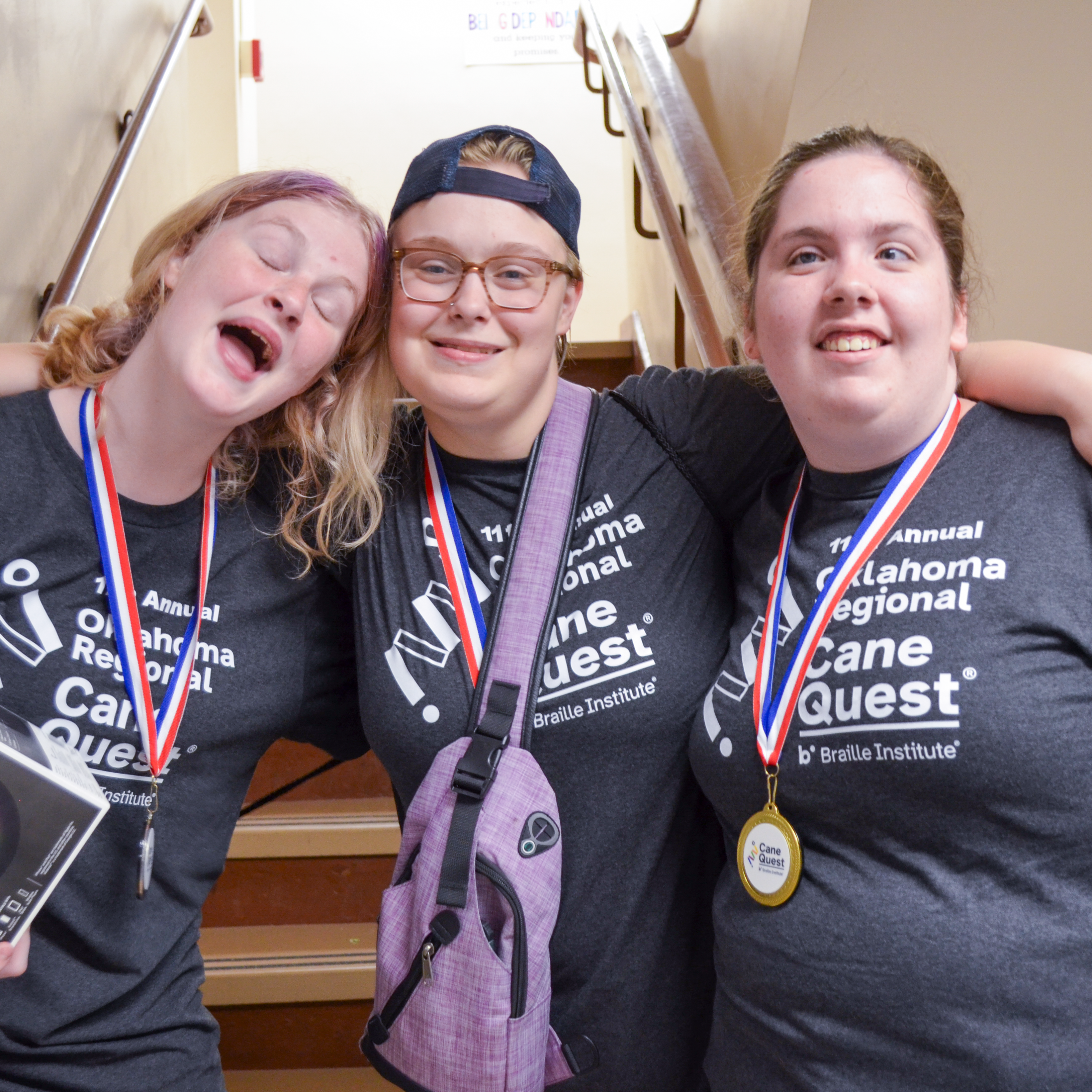 Three young girls with Cane Quest tee shirts and metals around their necks, smile big for the camera. 