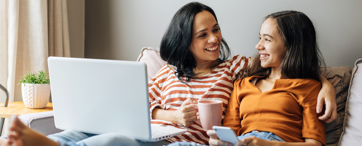 A woman and a child sit smiling at each other in front of a laptop.