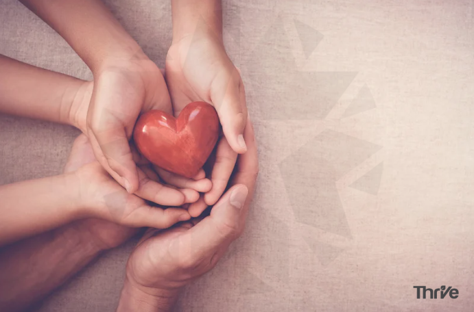 three sets of hands holding a wooden heart